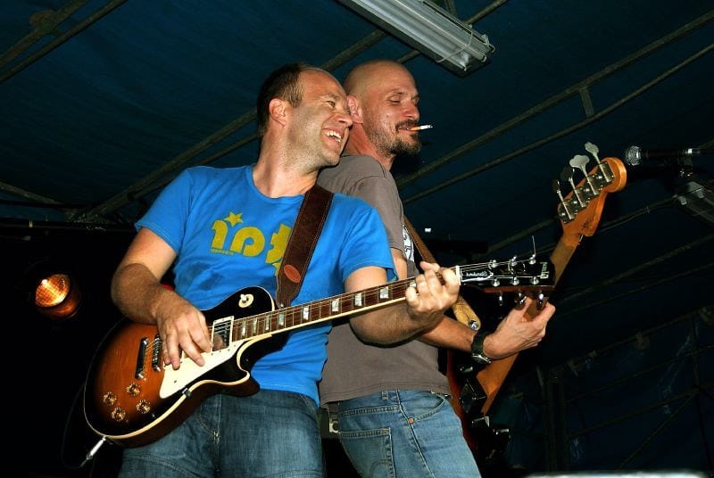 Ben Crabbé, energetic and smiling, playing guitar on stage, embodying the spirit of Belgian rock.