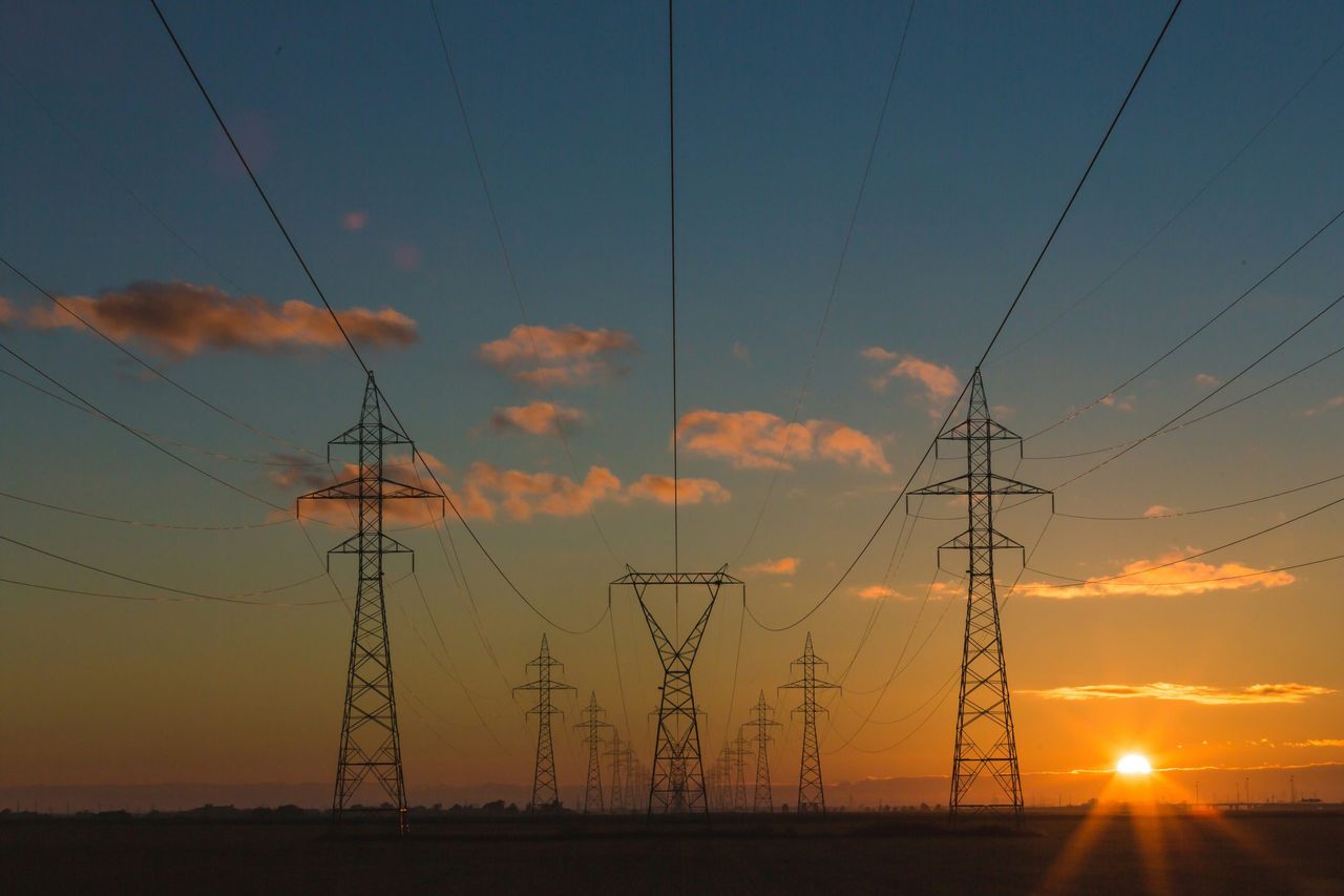 Pylônes d'électricité se découpant contre un coucher de soleil, reflétant l'engagement de Tony Beeuwsaert dans l'optimisation énergétique.